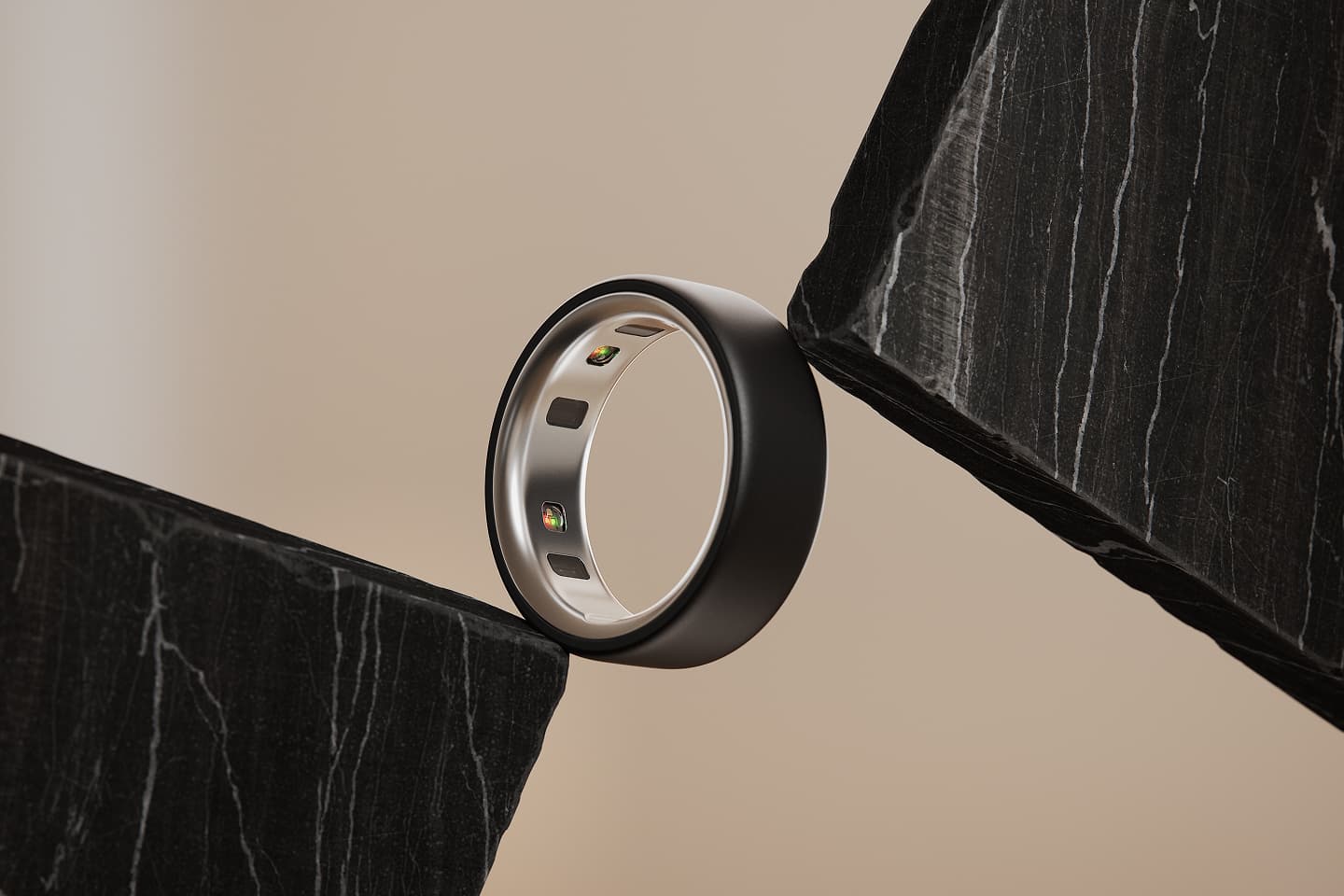 An Oura ring, embedded with sensors, is balanced between two dark marble slabs against a warm beige background.