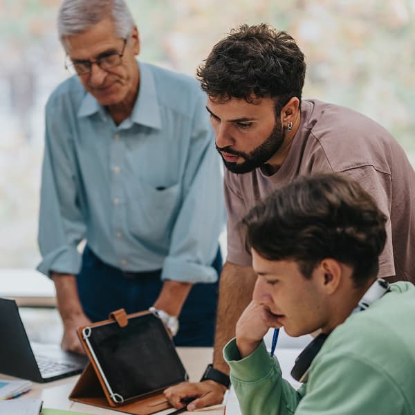 Three men focus on documents and a tablet at a table, suggesting a collaborative work environment. The mood is attentive and engaged.